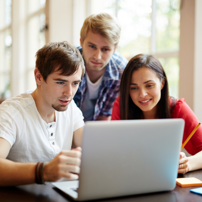 zdjęcie przedstawia trzech studentów pochylających się nad laptopem